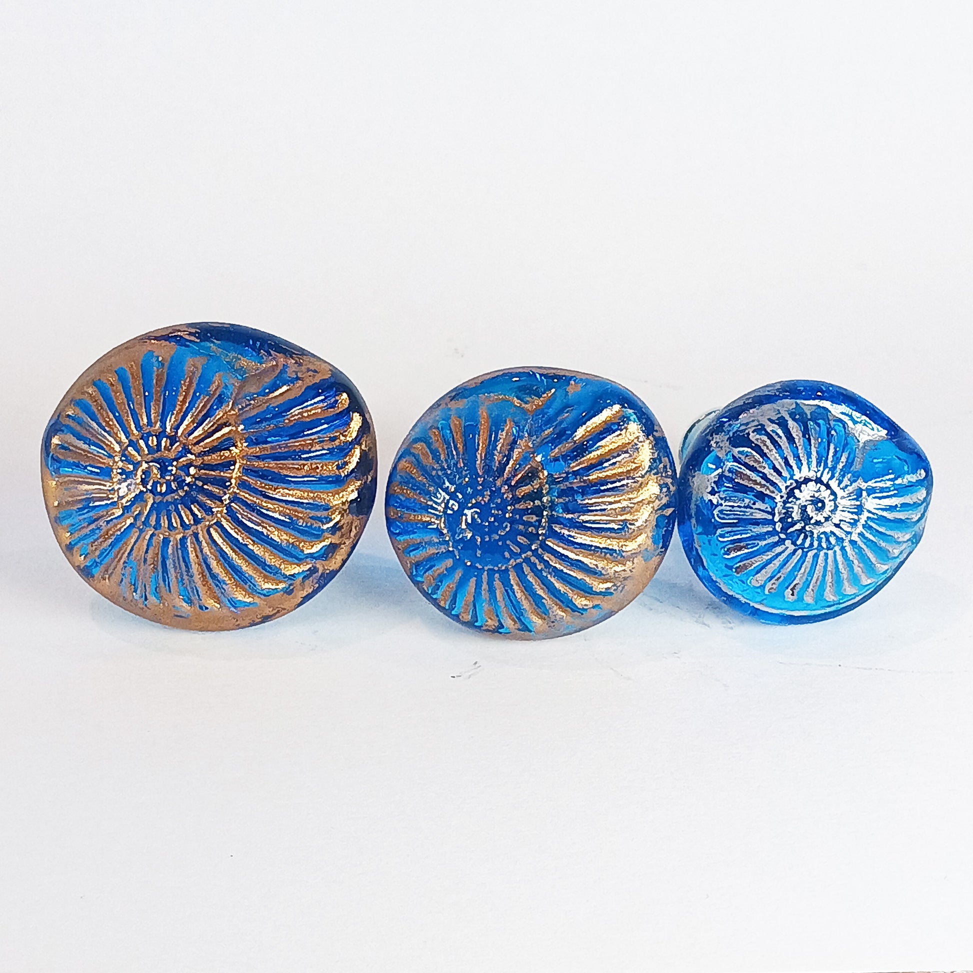 Three blue glass shell knobs with gold and silver textured accents